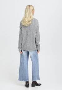 Pulover gri tricotat cu mâneci lungi, asortat cu blugi deschiși la culoare, cu picioare largi. Ținuta include pantofi negri lucioși. Design simplu.