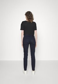 Camiseta negra de manga corta combinada con pantalones ajustados azul marino y zapatillas blancas, vista desde la parte de atrás. Diseño simple con detalles mínimos.