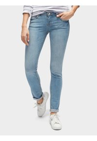 Jeans skinny de mezclilla azul claro con cintura media, diseño de cinco bolsillos, desgaste sutil y puños enrollados, combinados con zapatillas blancas.