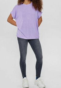 Lila oversized t-shirt med korta ärmar, kombinerad med mörkgrå skinny jeans och vita sneakers. Slät tyg, enkel design.