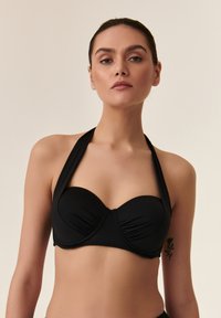 Black bikini top with a halter neck design, featuring a ruched front and smooth cups. Made of stretchy swim fabric for comfort.