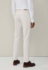 Witte, slim-fit broeken met achterzakken, gecombineerd met donkerbruine suède schoenen. Glad textuur, op maat gemaakt ontwerp en minimalistische stijl.