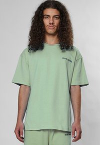 Túlméretezett menta zöld póló, puha pamutból készült. Rövid ujjú és a bal mellen "9N1M SENSE." felirat található.