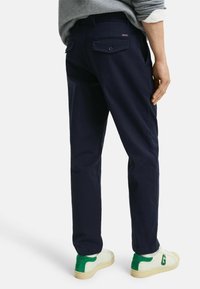 Pantalon bleu marine en coton avec une coupe droite, doté d'une poche arrière à bouton, associé à des sneakers blanches avec des accents verts.