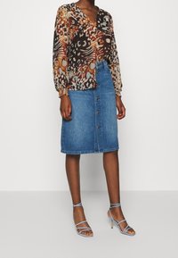 Mönstrad blus med långa ärmar, i nyanser av brunt och orange. Jeanskjol med knappar i fronten, i kombination med ljusblå klacksandaler.