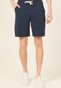Granatowe szorty z mieszanki bawełny z elastycznym pasem i sznurkiem, z bocznymi kieszeniami i prostym krojem. Noszone z białymi trampkami.