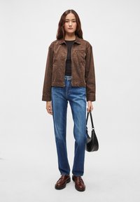 Ruda leopardo rašto striukė, juodas viršus, mėlyni tiesūs džinsai ir rudi masyvūs batai. Laiko mažą juodą rankinę.