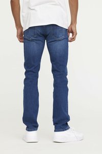 Jean en denim bleu foncé avec une coupe droite, dotés de poches arrière et d'une légère décoloration. Portés avec des baskets de sport blanches.