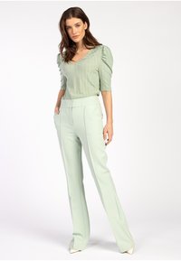 Hellgrüner gerippter Oberteil mit Puffärmeln, kombiniert mit mintgrünen taillierten Hosen; slim fit und elegante Silhouette mit eleganten spitzen Schuhen.