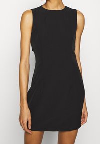 Robe noire sans manches avec un col rond, silhouette ajustée et texture lisse. Les coutures latérales créent une légère forme.