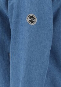Blauer Stoff mit einem strukturierten Muster zeigt auf der Seite einen kreisförmigen grauen Fleck, der mit "ZIGZAG" beschriftet ist, und hebt damit das Designdetail hervor.