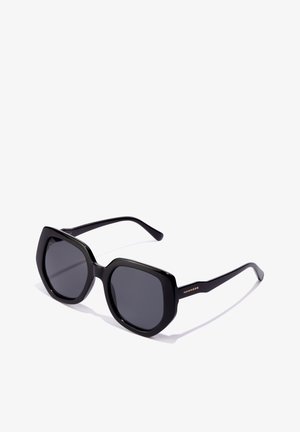 Melni saules brilles ar izteiktu kvadrātu rāmi, gludu plastmasas materiālu, tumšiem tonētiem stikliem un zelta akcentiem uz kājām.