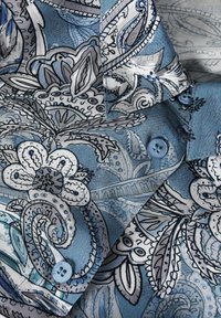 Camisa azul con patrones que presenta intrincados diseños florales y de cachemira en negro y blanco, con botones de color azul claro y una textura de tela suave.