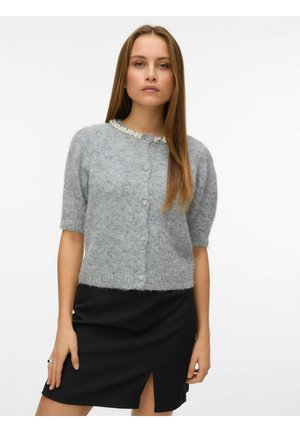 Cardigan en tricot gris à manches courtes, en tissu texturé, avec fermeture à boutons et accents en perles sur le col, porté sur une jupe noire.