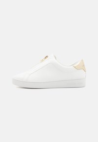 Baskets blanches en cuir avec une fermeture éclair à l'avant, des accents en métal doré et une semelle texturée. Marque affichée sur le talon.