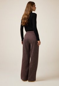 Spodnie o szerokich nogawkach z bordowego, teksturowanego materiału, z wysokim stanem i subtelnymi kieszeniami w szwach bocznych, zestawione z dopasowanym czarnym topem.