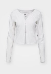 Top de manga larga blanco con canalé que presenta un cremallera frontal, cuello redondo y detalle de logo. La tela tiene un acabado texturizado.