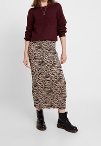 Pull en maille marron, associé à une jupe midi beige à rayures zébrées noires, porté avec des bottes de combat noires à lacets.