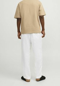 Beżowa bawełniana koszulka z krótkim rękawem, w zestawieniu z luźnymi białymi spodniami lnianymi. Włożona z czarnymi butami na naturalnej korkowej podeszwie.