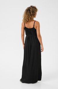 Robe maxi noire sans manches avec un dos smocké, des bretelles fines et une silhouette fluide qui atteint les chevilles.