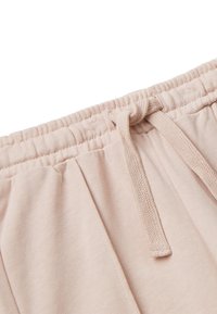 Beige kalhoty s elastickým páskem mají stahovací šňůrku, měkkou texturu, skladby v přední části a žádné viditelné vzory nebo kovové prvky.