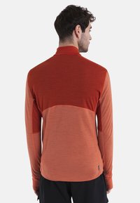Camisetta rossa a maniche lunghe con un motivo testurizzato, caratterizzata da una sfumatura di colore che va da tonalità più scure a più chiare, e un design a collo alto.