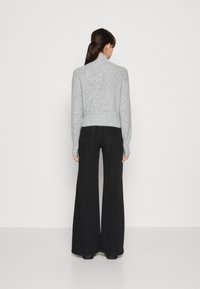 Suéter cinza de malha com gola alta e textura canelada, combinado com calças largas de cintura alta pretas. Design simples, sem padrões visíveis.