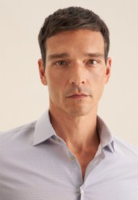 Helles blaues Button-Down-Hemd mit einem dezenten geometrischen Muster, Kragen und kurzen Ärmeln, ausgestattet mit cremfarbenen Knöpfen und einer glatten Baumwolltextur.