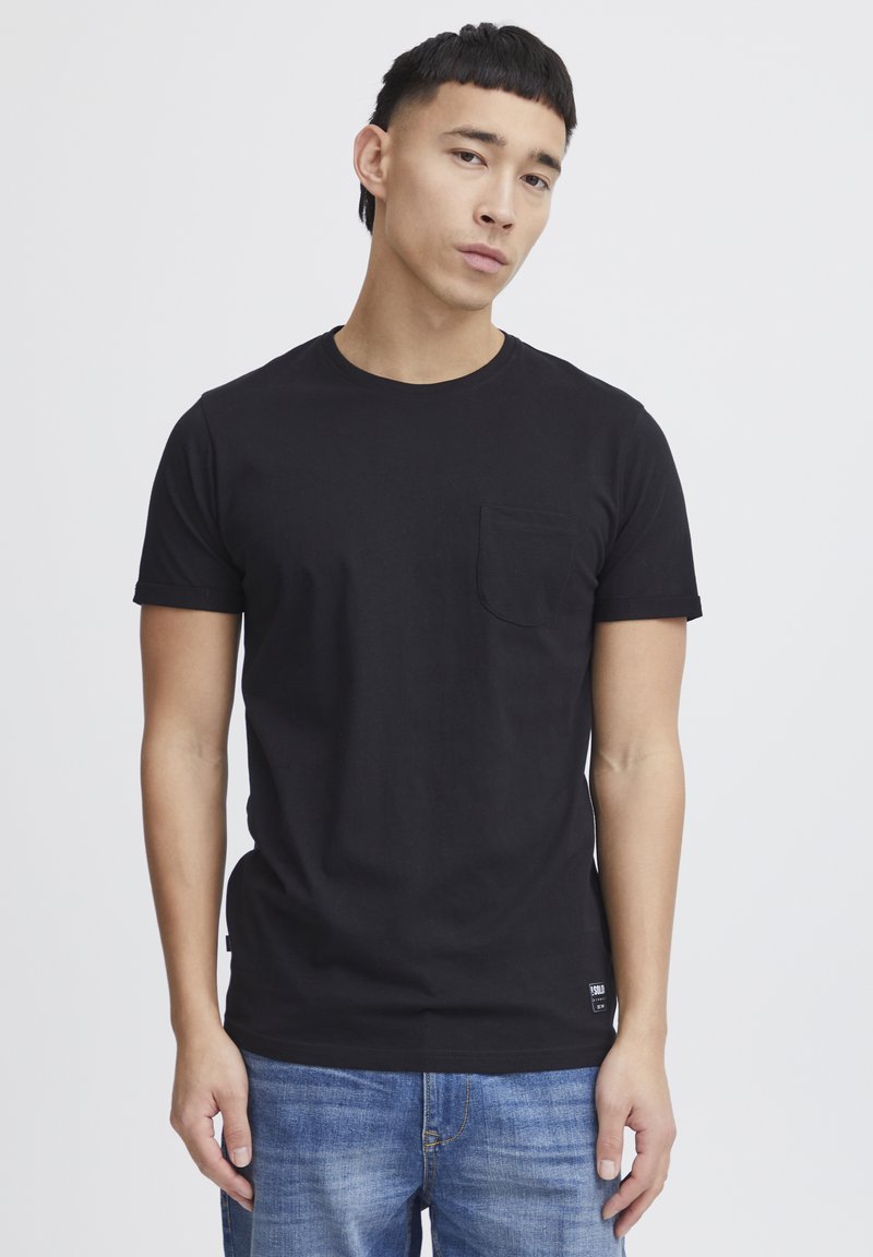 T-shirt en coton noir à manches courtes, col rond et poche poitrine. Associé à un jean en denim bleu. Présente une étiquette sur l'ourlet.
