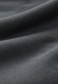 Tessuto grigio scuro con una texture liscia e un delicato motivo a coste, piegato in onde morbide. Materiale leggero ed elastico.