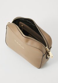 Sac à main en cuir marron avec une forme arrondie, fermeture éclair dorée et logo. L'intérieur comprend plusieurs compartiments, dont une section zippée.