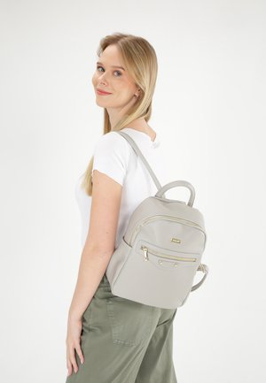 Světle šedý batoh s umělou kůží a zlatými detaily, kulatý tvar, přední kapsa na zip a polstrované popruhy, nošený na zádech.