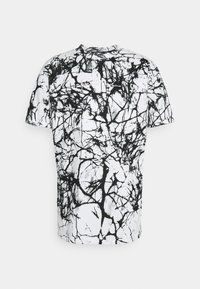 T-shirt à manches courtes en mélange de coton, présentant un motif abstrait noir et blanc avec un effet marbré sur un fond clair.