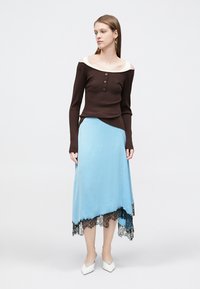 Καφέ μακρυμάνικη μπλούζα με ριπ υφή και εκρού λεπτομέρειες έξω από τον ώμο, με τρία κουμπιά. Ανοιχτό γαλάζια ασύμμετρη φούστα με μαύρη δαντέλα στο τελείωμα. Λευκά παπούτσια με τακούνι.