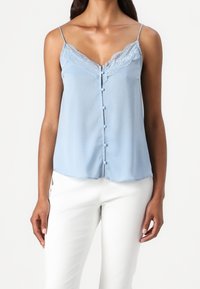 Haut sans manches bleu clair avec un bord en dentelle et fermeture à boutons. Fabriqué en tissu doux, il présente une coupe décontractée et un ourlet arrondi.