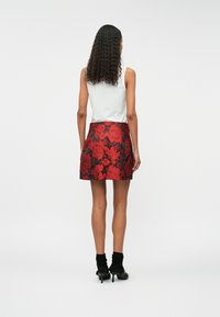 Blomstermønstret miniskjørt i rød og svart stoff, med en figursydd midje og en utsvingt silhuett. Brukt sammen med en hvit ermeløs topp og svarte hæler.