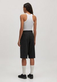 Schwarze, strukturierte Shorts mit Mittelhochbund und Taschen, kombiniert mit einem weißen Tanktop. Weiße Socken und schwarze Schuhe runden den Look ab.