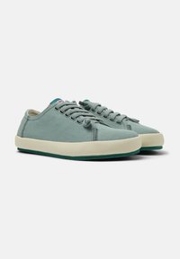 Sneakers in tela verde con una finitura testurizzata, suola in gomma bianca sporca e lacci coordinati. Presentano dettagli di cucitura e un piccolo tag con logo.