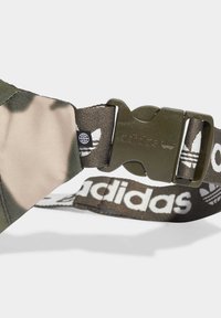 Olivgrön plastspänne på camoflagetygrem med vit Adidas-text och logotyp på justerbart tygbälte.