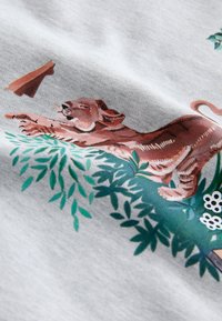 Hall kangas, millel on lõbus lõvikutsika joonistus, ümbritsetud roheliste lehtede ja valgete lilledega, pruunide ja roosade detailidega.