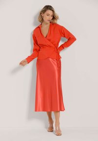 Rote Bluse mit langen Ärmeln und Bindedetail, kombiniert mit einem glatten, glänzenden roten Satin-Midi-Rock und klaren blockabsatz Sandalen.