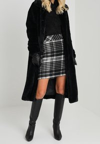 Schwarzer Kunstpelzmantel, strukturiert, oversized; figurschmeichelnder schwarzer Rollkragenpullover; grauer karierter Minirock; knielange schwarze Stiefel; schwarze Handschuhe.