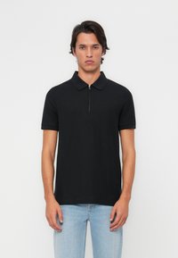 Melna īsām piedurknēm polo krekls ar rāvējslēdzēja apkakli, izgatavots no gluda auduma. Piegriezums ir pieguļošs, minimālistisks dizains, bez redzamām rakstainēm vai akcentiem.