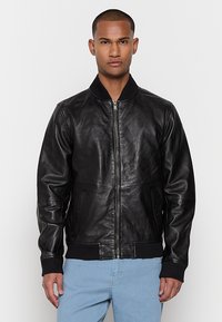 Giubbotto bomber in pelle nera con polsini e colletto a costine, chiusura con zip e tasche laterali. Texture liscia e design aderente.