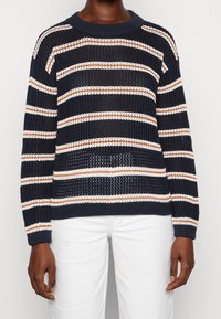 Sweter w marynarskie paski z otwartym splotem, w poziome paski w kolorze kremowym i rdzy. Klasyczny okrągły dekolt i ściągacze na rękawach.