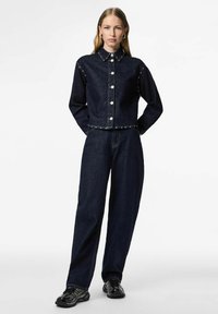 Denimjakke og bukse i mørk vask. Jakken har metallknapper og en kortere design. Begge har en avslappet passform og minimalistiske detaljer.