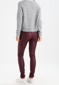 Szary dzianinowy sweter z okrągłym dekoltem, zestawiony z bordowymi, obcisłymi spodniami ze sztucznej skóry. Całość uzupełniają białe sneakersy.