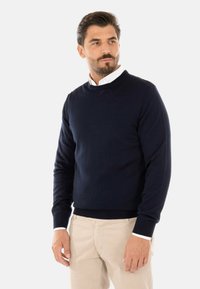 Maglione navy blue a girocollo con maniche lunghe, polsini e orlo a costine, realizzato in un tessuto morbido, indossato sopra una camicia bianca con colletto.
