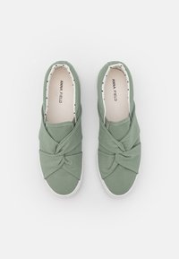 Zapatos slip-on de tela verde menta con un diseño anudado en la parte superior, suela de goma blanca y un forro liso de lunares en blanco y negro.