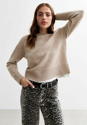 Pull en maille beige avec un ourlet et des poignets côtelés, associé à un pantalon taille haute à imprimé léopard et une ceinture noire. Tissu texturé visible.
